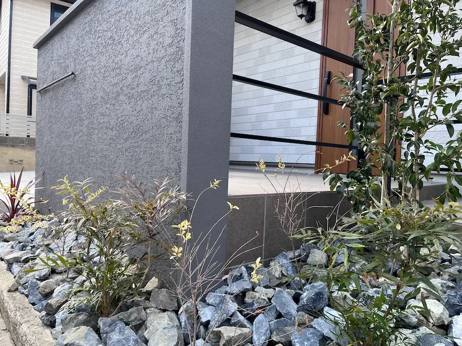 玄関前の道路沿いに続くロックガーデンと、プライバシーを守る造作門柱。自然素材とモダンな建材が調和したファサード。