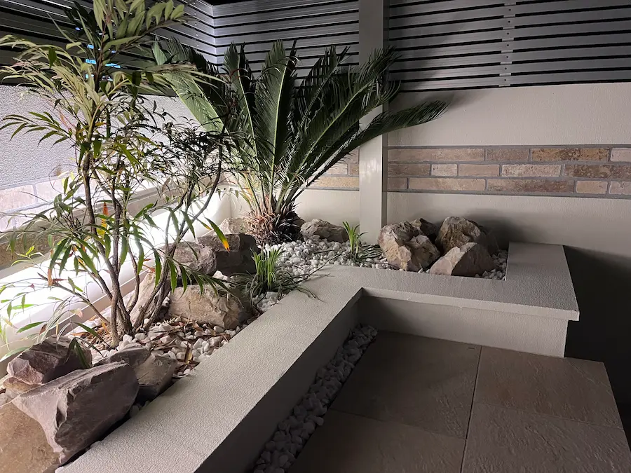 スポットライトで照らされた夜のロックガーデン。樹木の影が外壁に映り込み、昼間とは異なる表情を見せるライティング