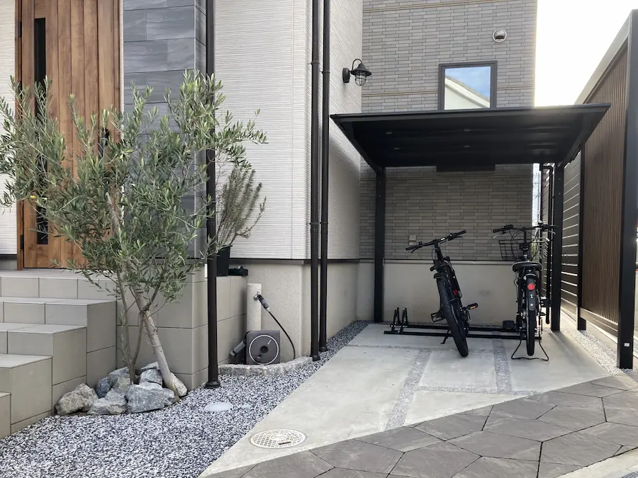 自転車が風にあおられて倒れてしまうお悩みを、サイクルポートと自転車専用ラックを設置して解決した施工事例。玄関周りが整理され、美観も保たれている。
