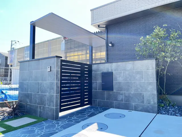 SOTORIE柏逆井のエクステリア施工実績2、船橋市I様邸。グレーのタイル門柱と黒い門扉、屋根付きのアプローチがあるモダンな外構。