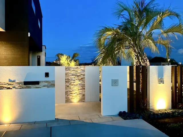 SOTORIE柏逆井のエクステリア施工実績5、市川市A様邸。ライトアップされたモダンな造作門柱とヤシの木がある夜の玄関アプローチ。