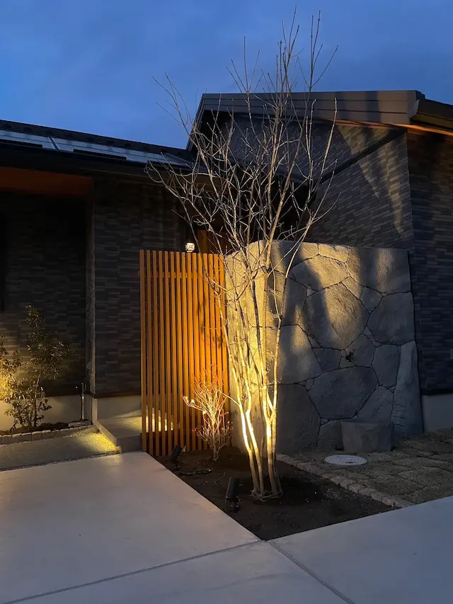 SOTORIE群馬伊勢崎のエクステリア施工実績1、モルタル調の石畳と木目フェンスを組み合わせたモダン外構。門柱は白系のタイル、右側にはグレーの石積み調ウォールを配置し、コントラストを強調したデザイン。