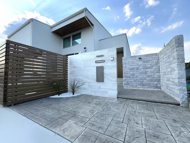 SOTORIE群馬伊勢崎のエクステリア施工実績3、木目調の縦格子とゴツゴツとした石積み風モルタル造形ウォール、シンボルツリーがアップライトで照らされたモダン外構の夜景。