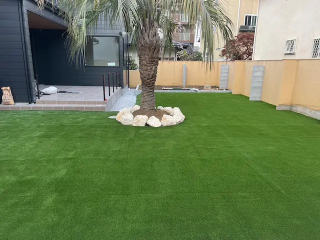 SOTORIE埼玉鶴ヶ島のエクステリア施工実績5、広々とした人工芝の庭と、中央に配置されたシンボルツリーのヤシの木