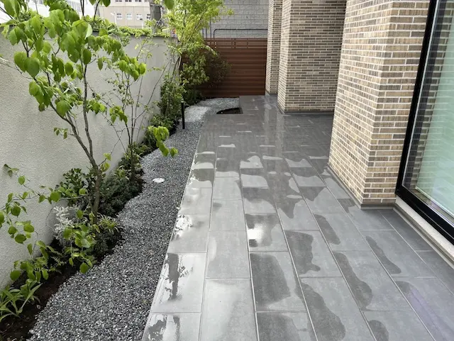 SOTORIE埼玉鶴ヶ島のエクステリア施工実績7、大判のグレータイルを敷いたテラスと、白い壁に沿った植栽スペース