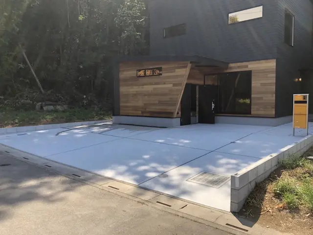 SOTORIE埼玉鶴ヶ島のエクステリア施工実績8、木目調の外壁がアクセントの住宅と、イエローのポストが映えるのコンクリート敷きの広々とした駐車場